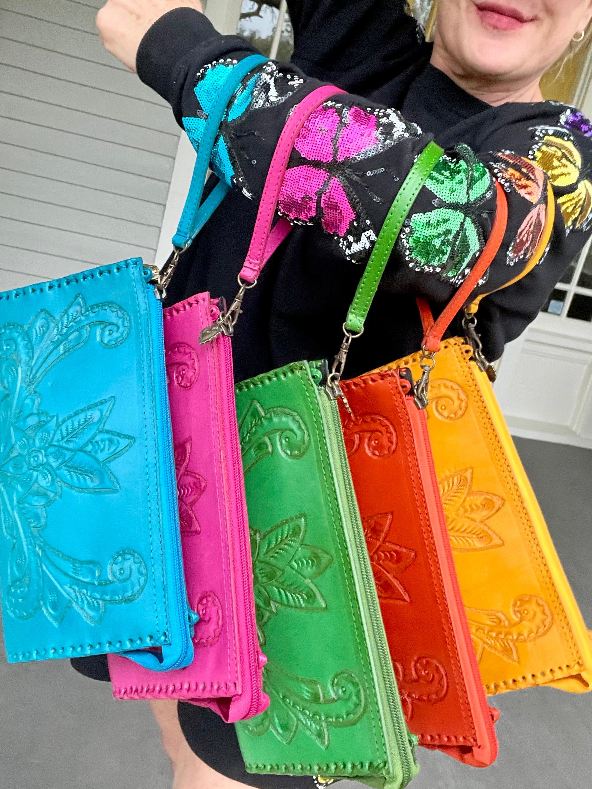 Five colorful embroidered leather hand bags held by a person with a blurred background