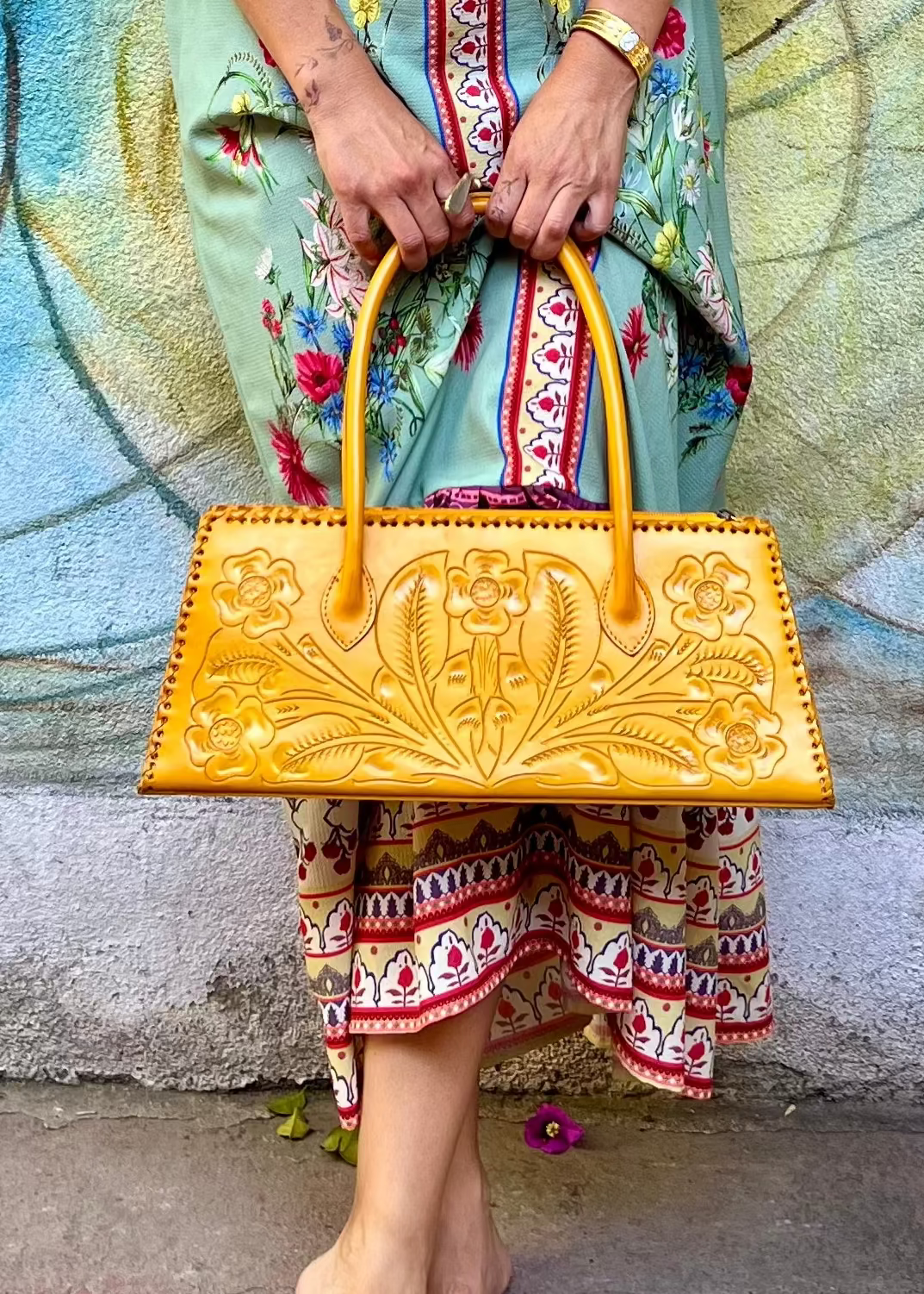 Person holding a yellow handbag in front of a colorful mural.