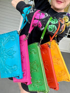 Five colorful embroidered leather hand bags held by a person with a blurred background
