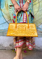Person holding a yellow handbag in front of a colorful mural.