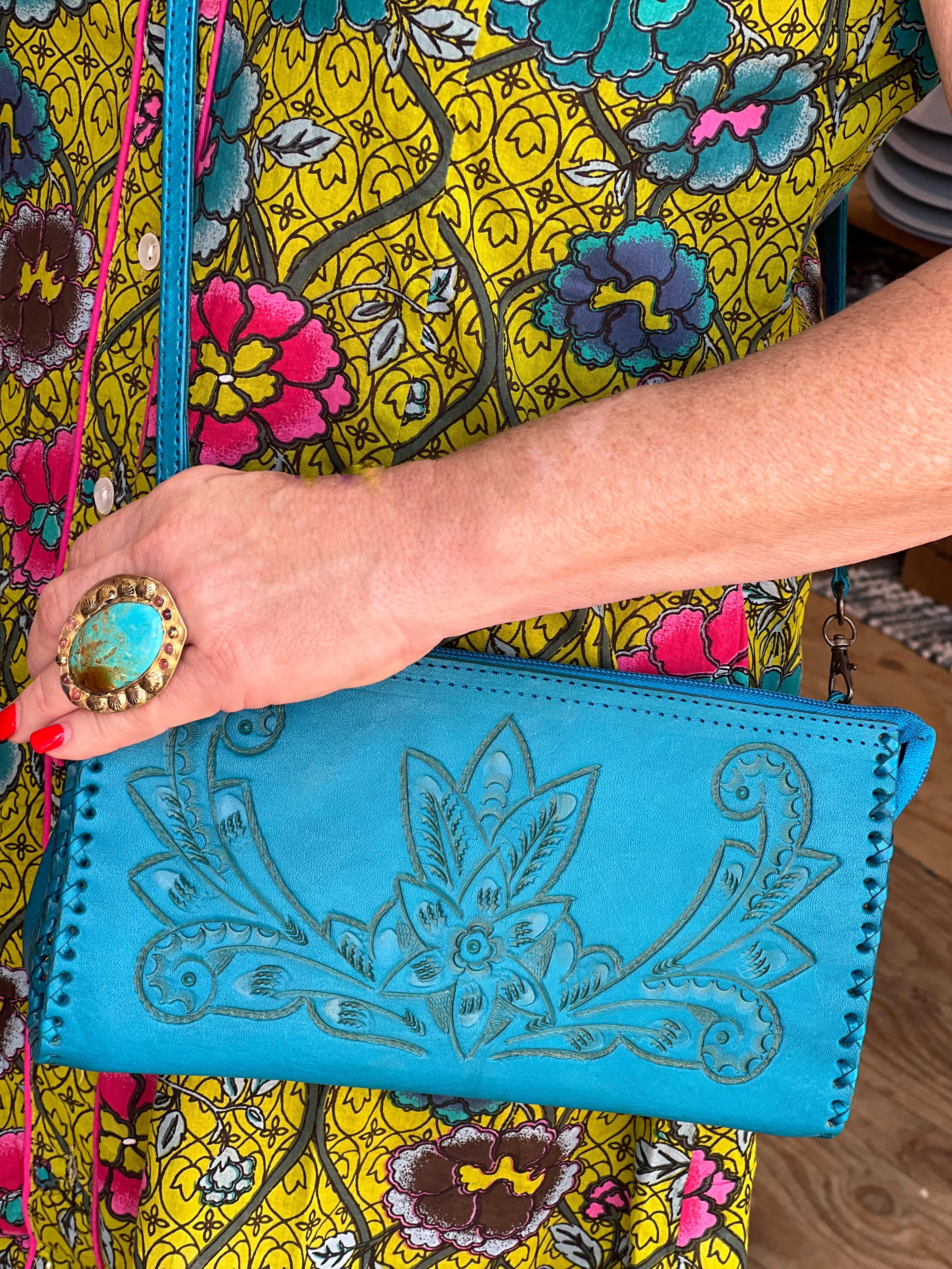 Person holding a blue clutch with intricate design, wearing a colorful floral dress.